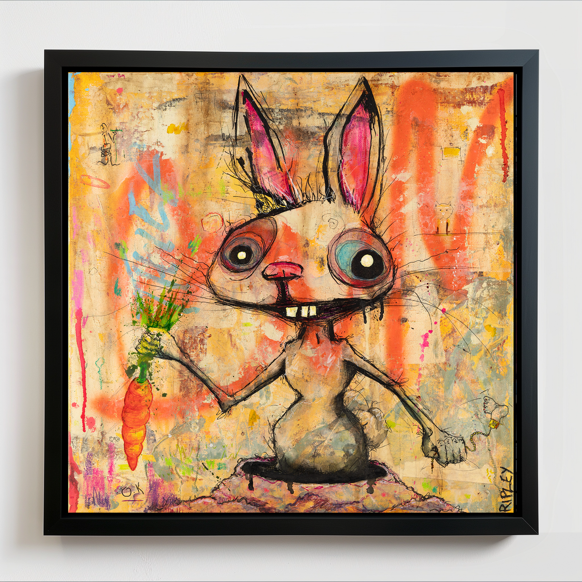 A framed square art print featuring a stylized cartoon rabbit holding a carrot, painted in bright orange, pink, yellow, and blue tones on a textured beige background, shown hanging on a light wall.