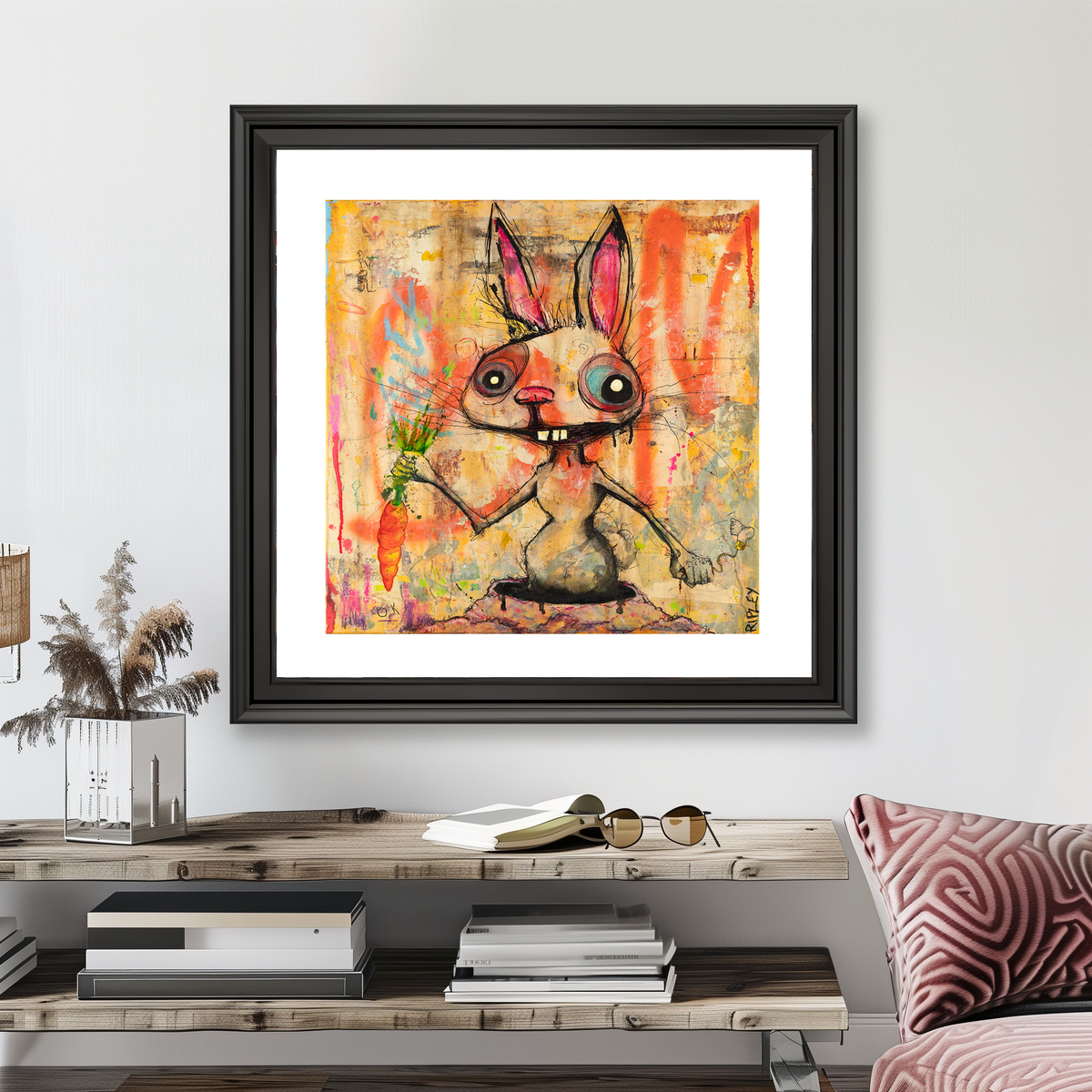 A framed art print featuring a whimsical cartoon rabbit holding a carrot, displayed on a light gray wall above a wooden console table with books and decor.