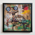 A framed mixed-media painting of a cartoon turtle with large blue eyes, hanging on a white wall. The artwork features a textured background in earthy tones with splatters, a red sun, and green accents, enclosed in a black frame.