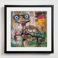A framed square art print featuring a whimsical painted turtle with oversized blue eyes, a patterned shell, and expressive brushstrokes in earthy tones, shown against a white wall.