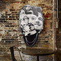“Parts of the Problem by Ripley, a layered grayscale portrait of Morgan Wallen on a brick wall above a café table.” A large black and white collage wall art piece featuring three overlapping male faces, mounted on a rustic brick wall above a small round table in a cafe-like interior.