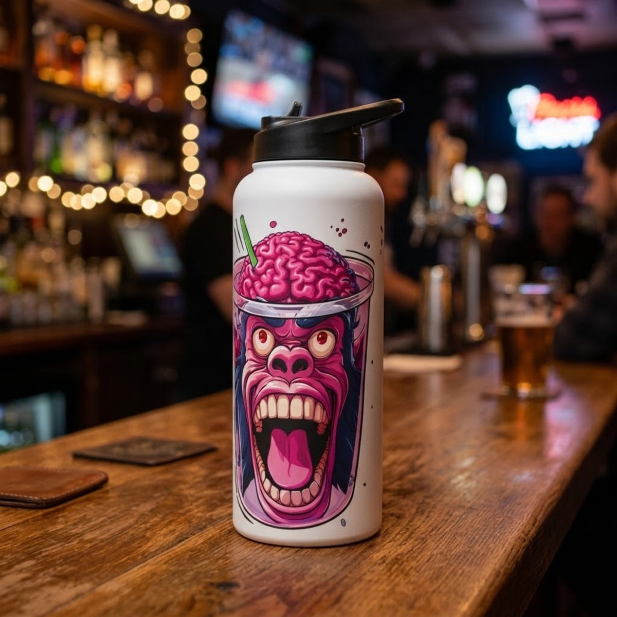 A white insulated water bottle with a black lid sits on a wooden bar counter in a blurred bar setting. The bottle features a graphic illustration of a screaming pink brain character. “Monkey Brain water bottle with a pink monkey and exposed brain graphic, standing on a wooden bar beneath warm lights.”