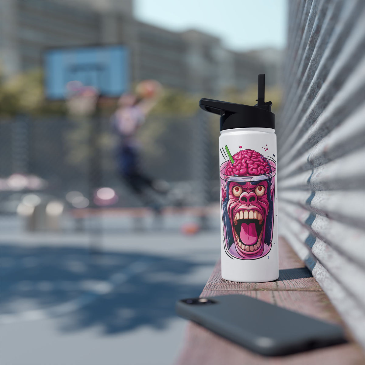 A white insulated tumbler with a black lid and straw stands on a wooden ledge outdoors. The tumbler features a colorful graphic of a screaming brain character in a drink.