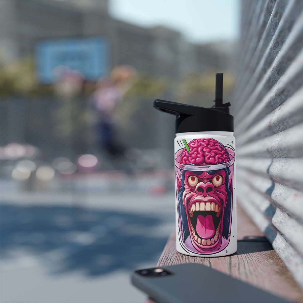 A white insulated tumbler with a black lid and straw, featuring a colorful cartoon graphic of a screaming ape head with a pink brain, resting on a wooden ledge outdoors with a blurred urban background.