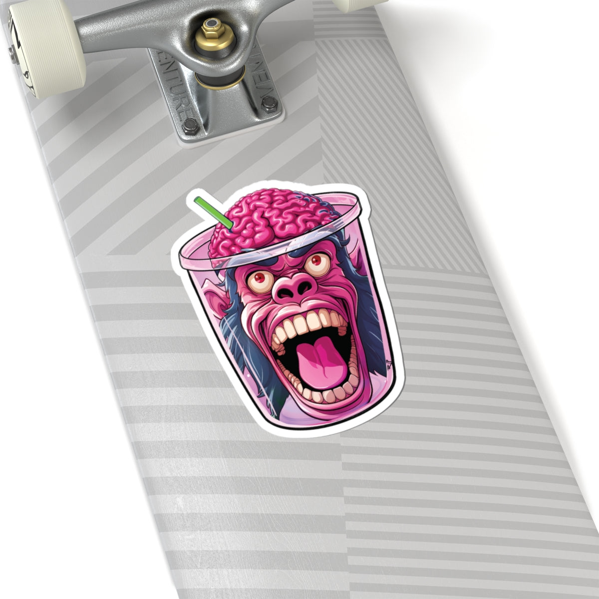 A die-cut sticker featuring a cartoon gorilla face inside a pink drink cup with a brain for a head and a green straw, shown applied to the deck of a skateboard.