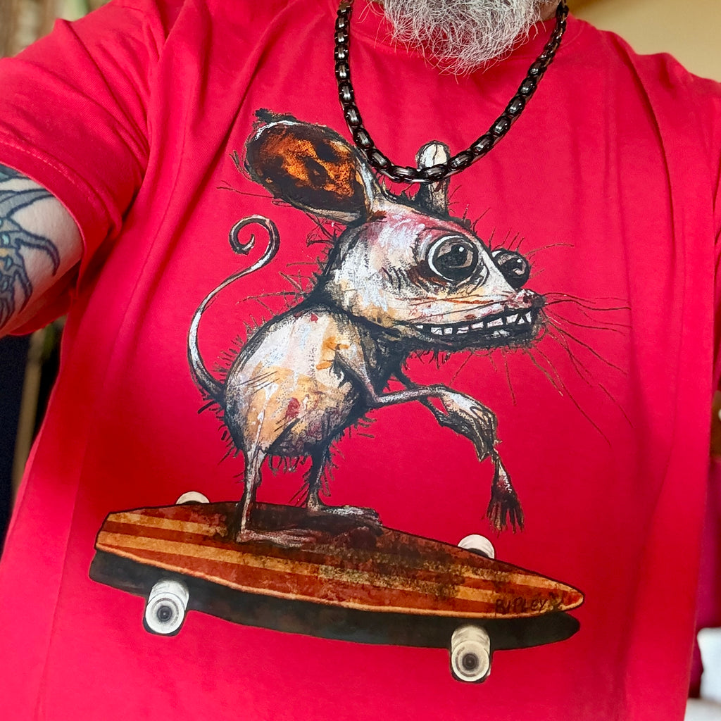 A close-up of a person wearing a bright red t-shirt with a graphic print of a creepy, large-eyed mouse balancing on a skateboard. The person also wears a black beaded necklace.