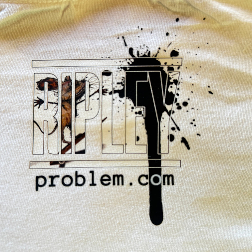 A close-up of a white fabric surface featuring a graphic print with the text 'ripleyproblem.com' and large stylized letters filled with black ink splatter and small illustrative details.