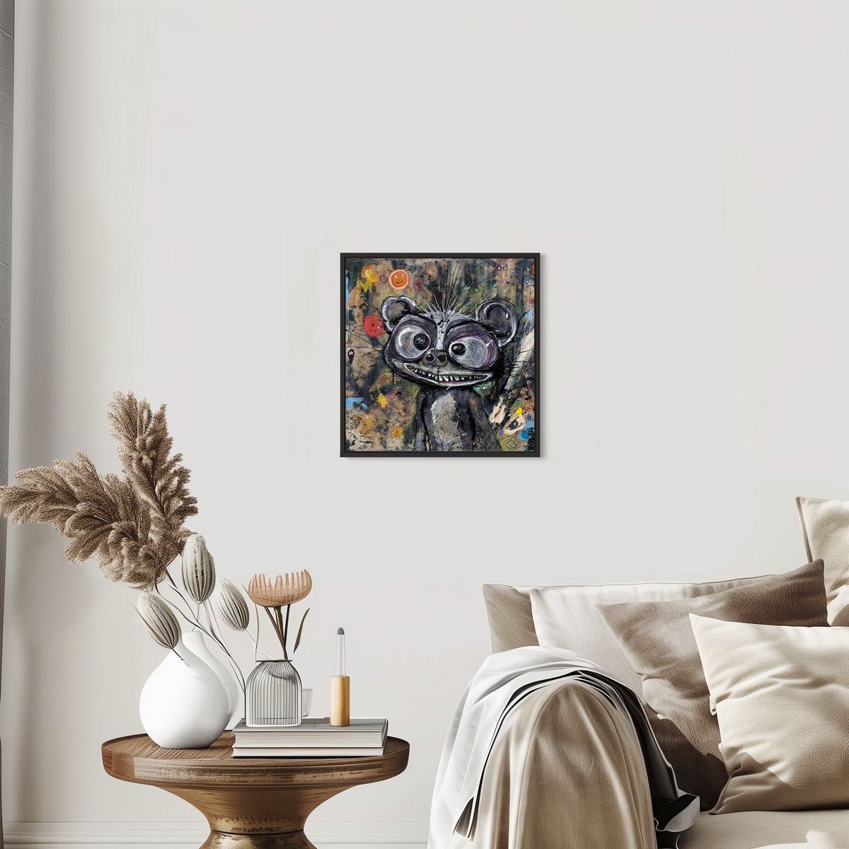 A framed abstract art print featuring a stylized black and white cartoon bear face with a red accent, displayed on a light gray wall above a bed in a styled bedroom setting.